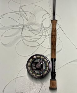 A fly rod with lots of extra line lying around it.