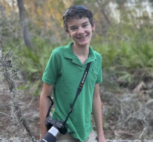 Boy smiling with a camera hanging from his shoulder.