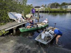 People on dock and shore unload debris from small boats.