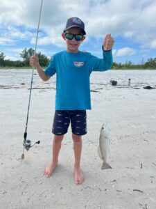 Boy standing on beach with a rod and reel and a fish he caught.
