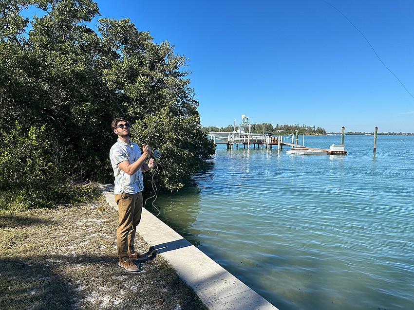 Young man holds a fly-casting rod by the bay.